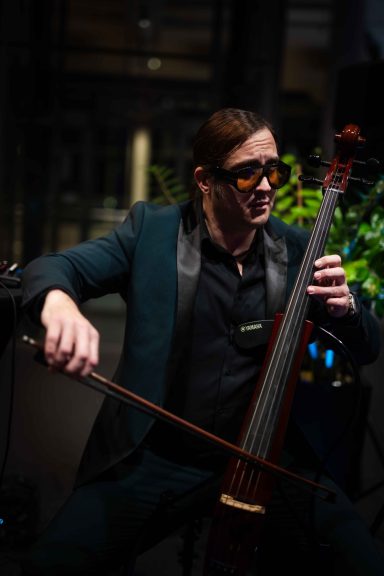 Mann in eleganter Kleidung spielt Cello in einem modernen, beleuchteten Raum.
